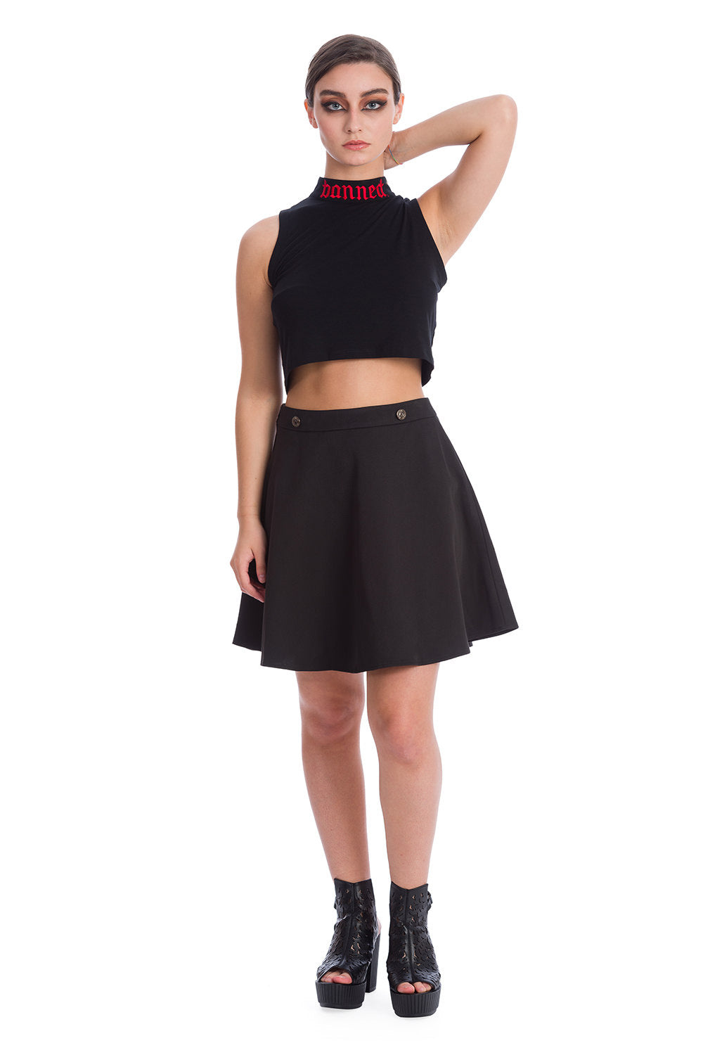 Model wearing black crop top with high neck with word 'banned' in red embroided on and a high waisted black a line skirt
