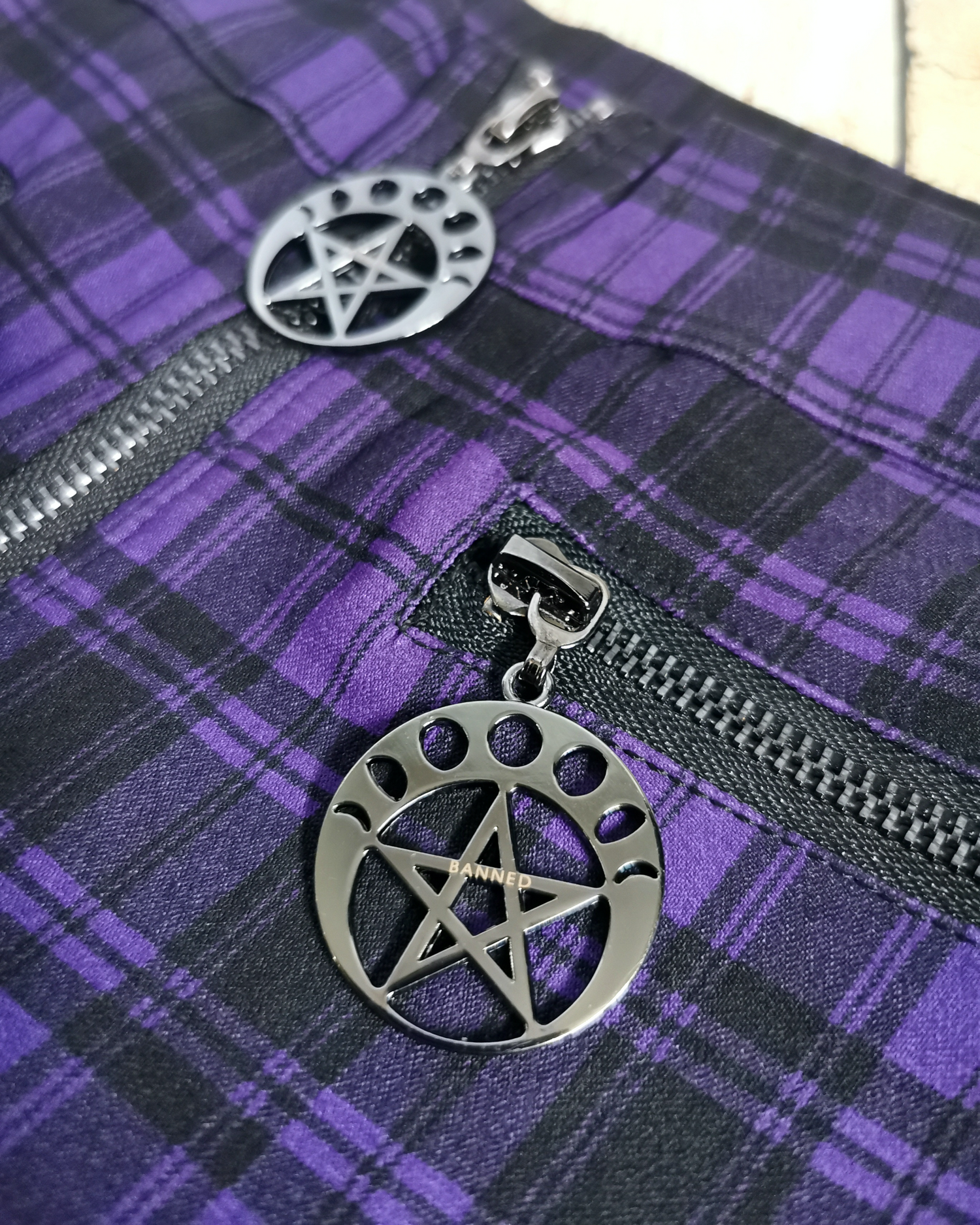 Detail shot of purple tartan trousers showing pentagram pendant 
