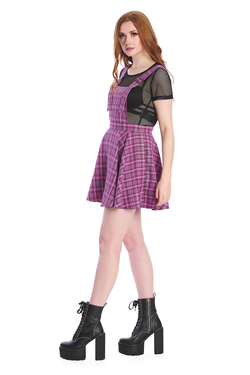 Model in a purple pinafore dress with black mesh crop top and black boots 