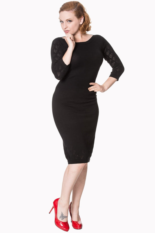 Model wearing black mid length fitted dress with sheer pattern sleeves