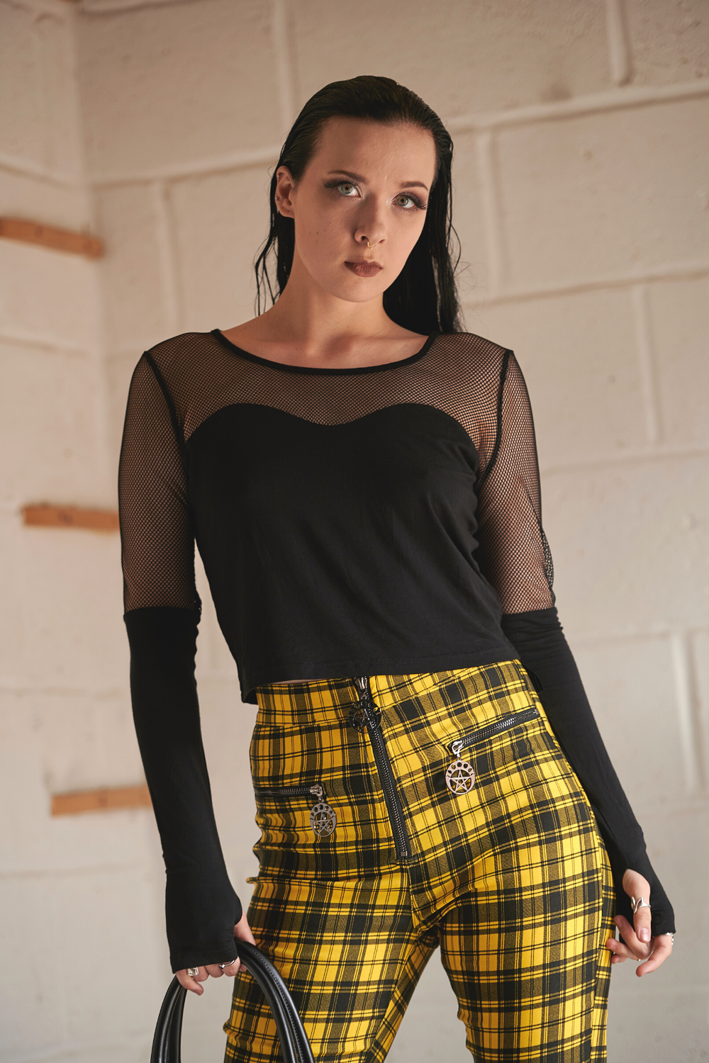 Grunge model wearing mesh long sleeve top with thumb holes in black and yellow tartan high wait trousers 