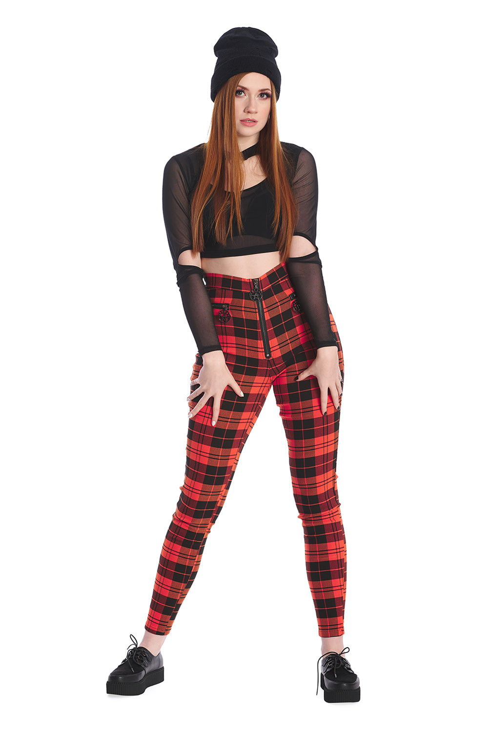 Model wears orange tartan high waisted trousers with a crop mesh top in black and beanie hat 